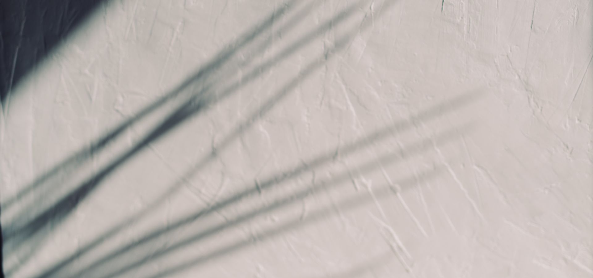 Diagonal window-blind shadows on a soft pink-grey surface