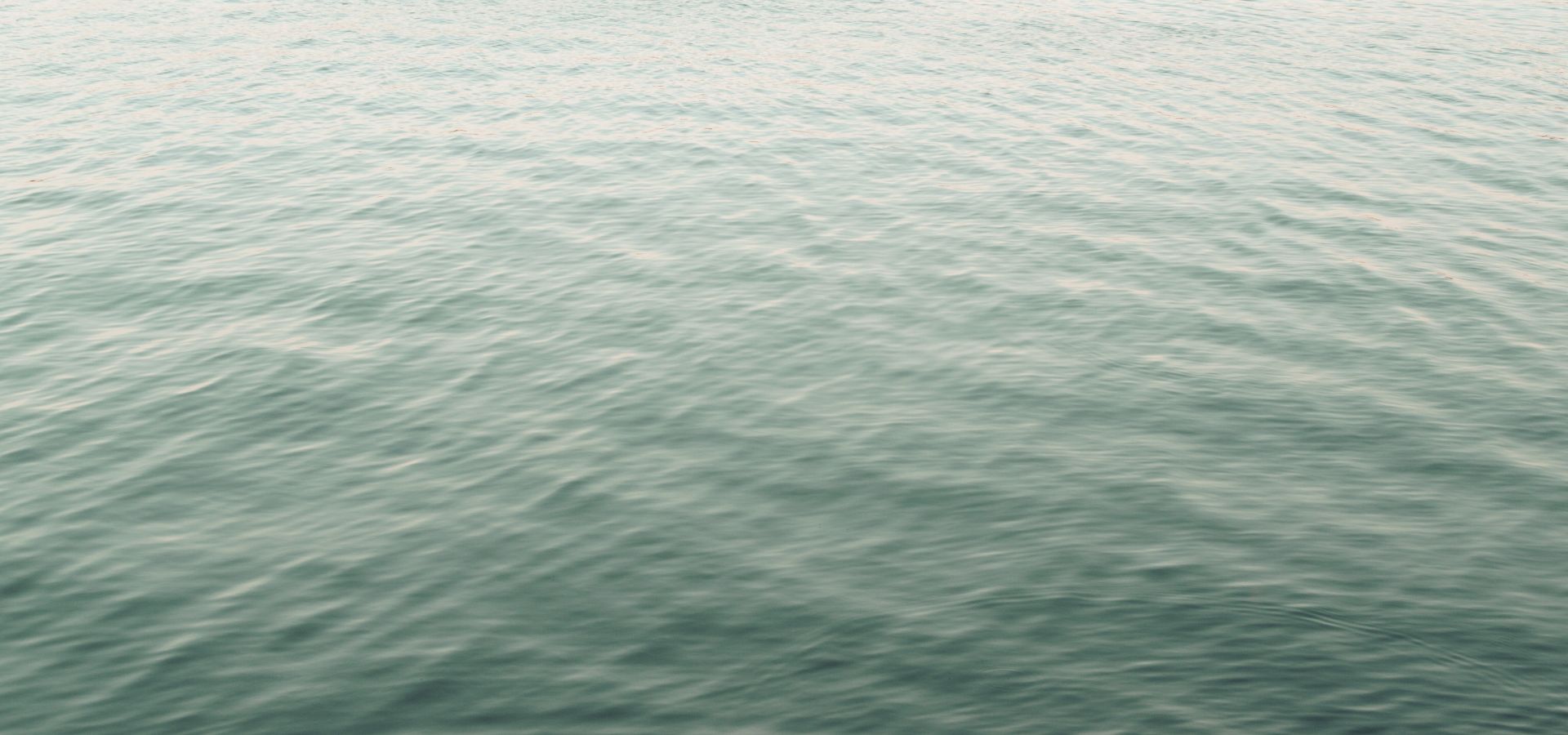 A calm teal water surface beneath a high horizon