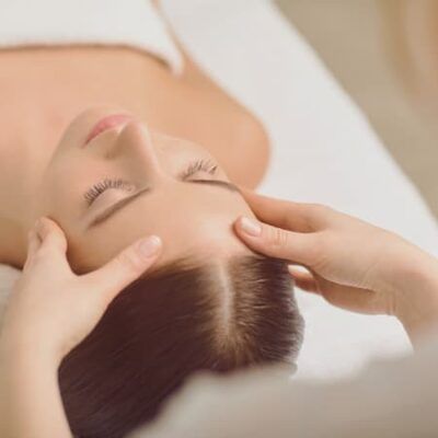 A practitioner massaging a reclining client's temples