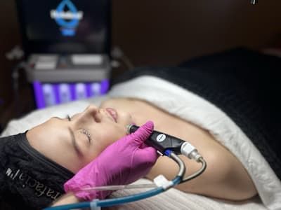 A practitioner guiding a HydraFacial handpiece across a reclining client’s cheek