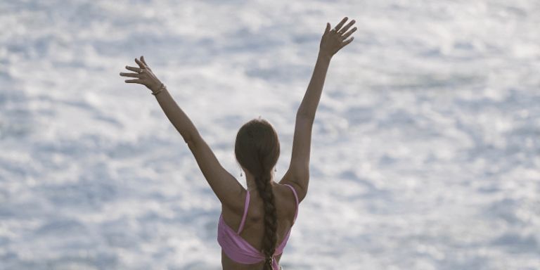 A woman standing at the shoreline with her arms raised