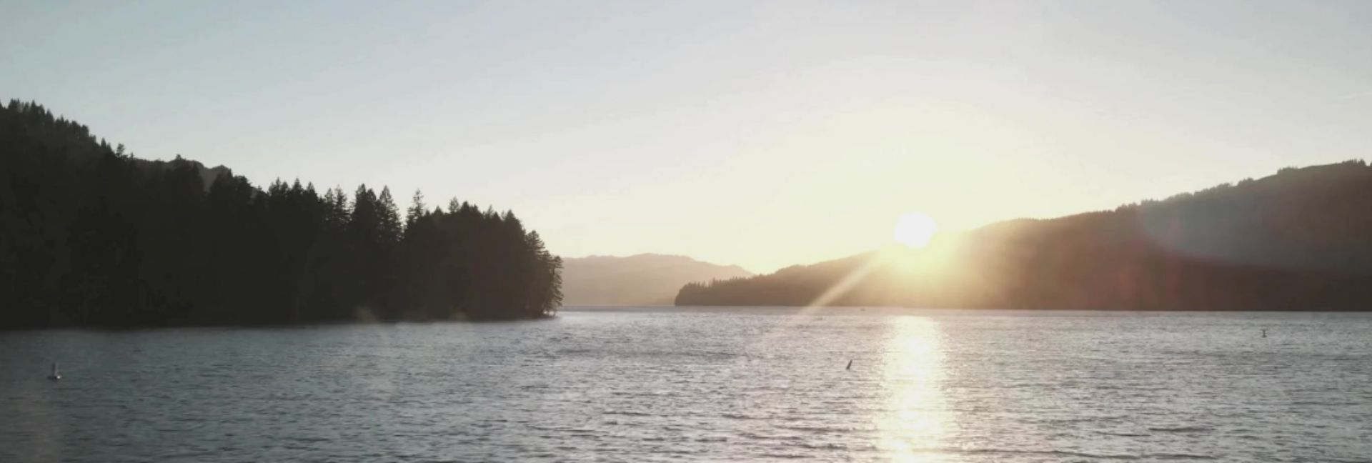 The sun low over open water, with wooded ridges on both shores