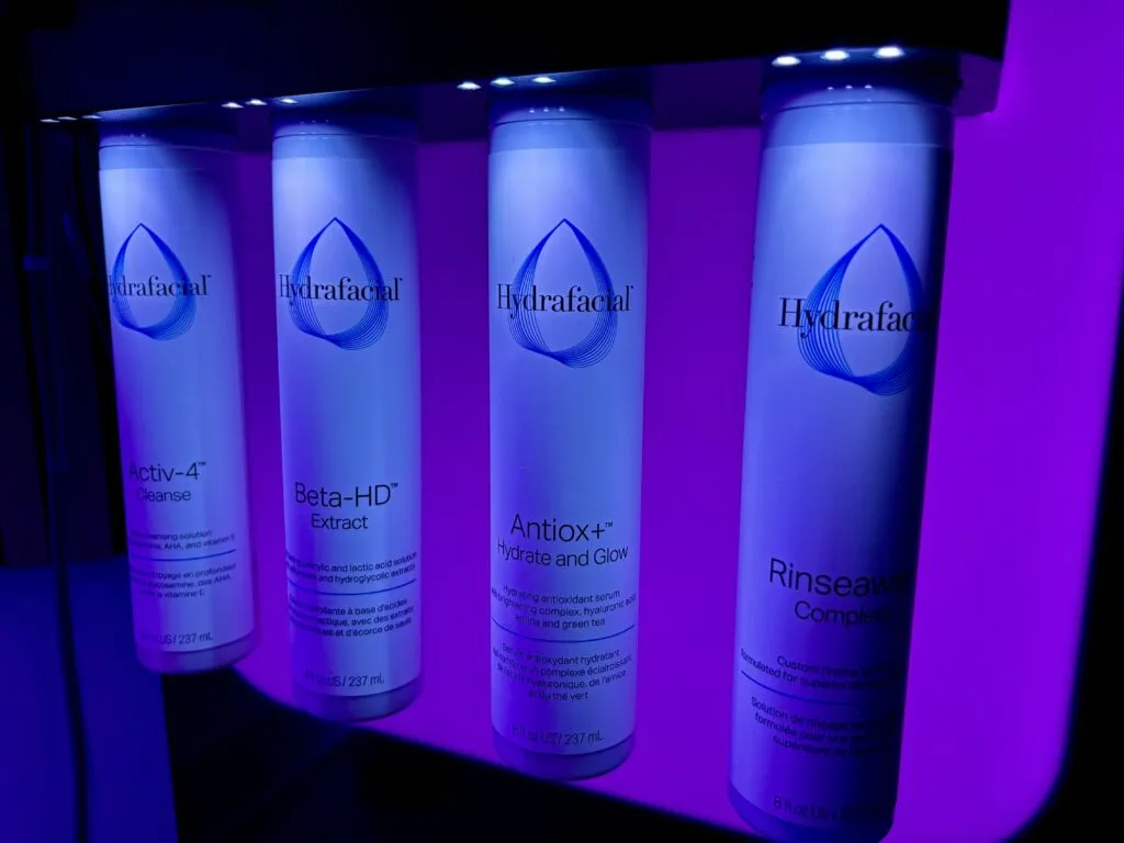 A close-up row of HydraFacial serum bottles under blue light
