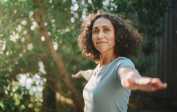 A woman standing outdoors among trees with her arms outstretched