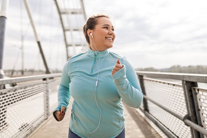 A woman running outdoors in a teal jacket