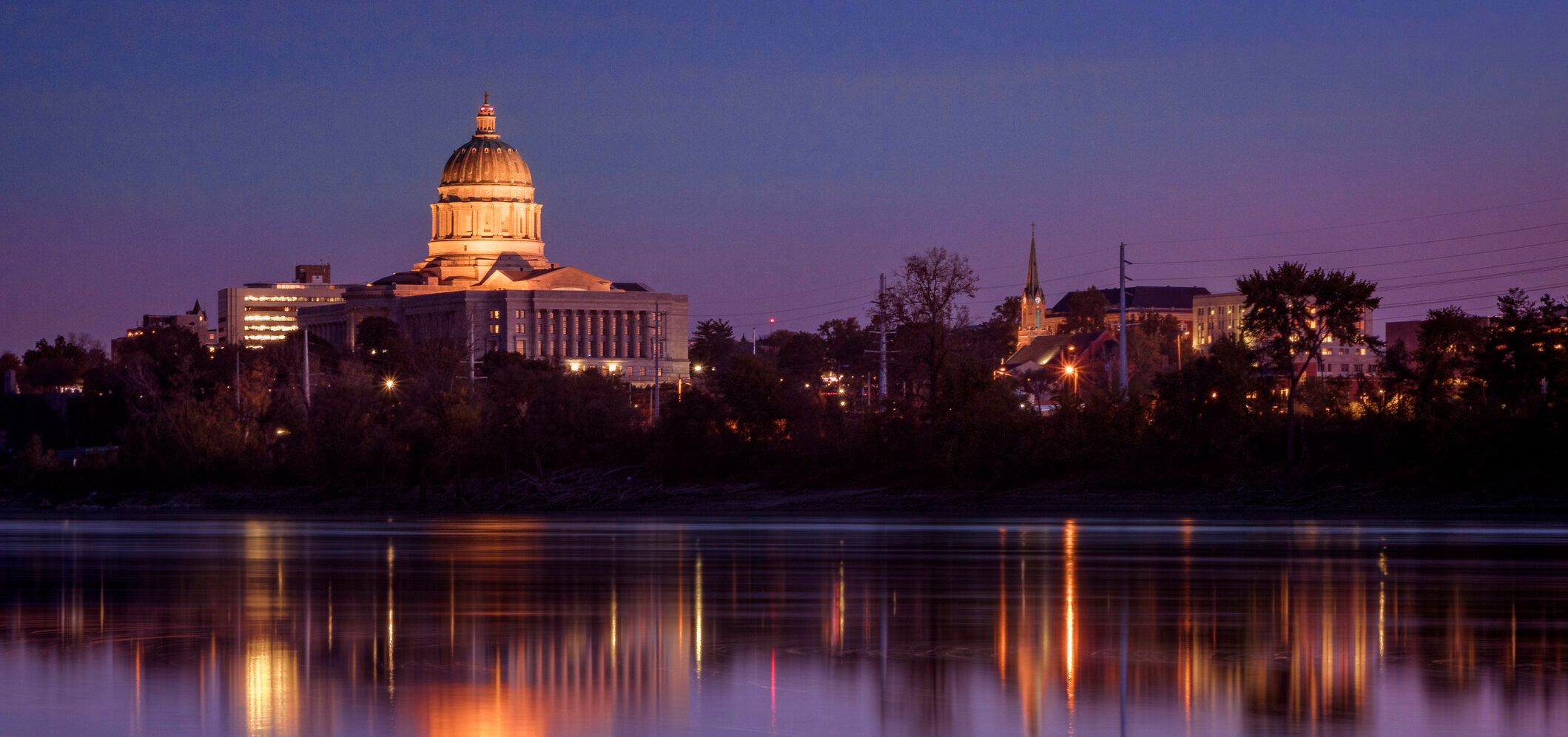 The Missouri State Capitol floodlit at dusk, reflected in the river