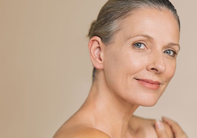 A woman with grey hair turning towards the camera against a warm backdrop