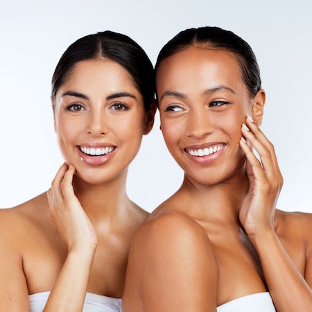 Two women smiling, each resting a hand against her own cheek