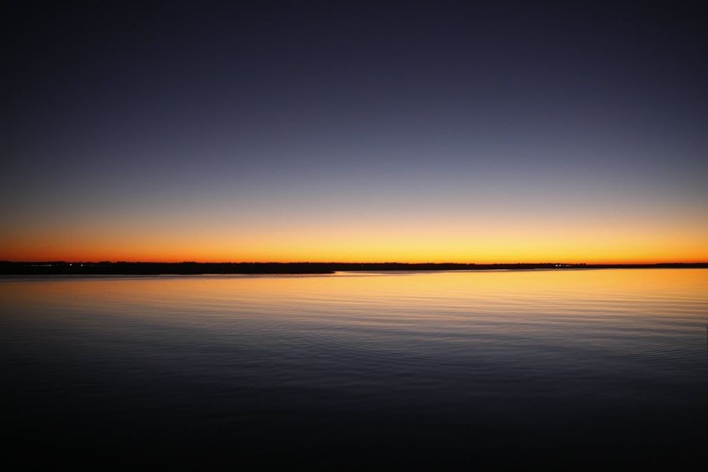 A calm sea under a blue and orange sky at sunset