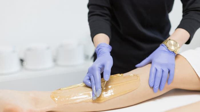 A practitioner spreading warm sugaring paste along a client’s lower leg