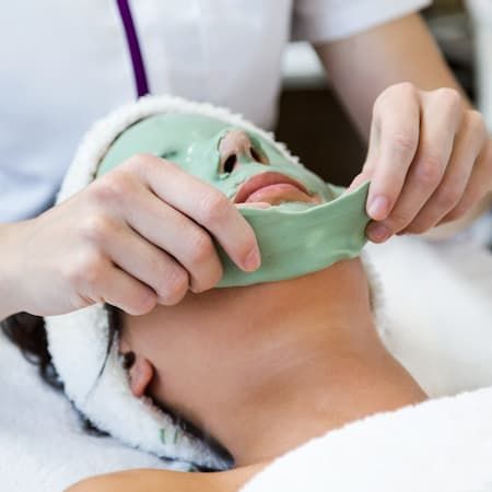 A practitioner lifting a green firming mask from a reclining client’s face